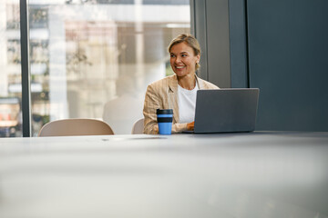 Female sales manager working on laptop while sitting the desk in modern coworking 