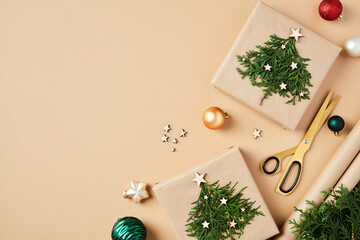 Flat lay Christmas composition with DIY Christmas gifts with fir branches, decorations, balls, scissors, wrapping paper on beige background.