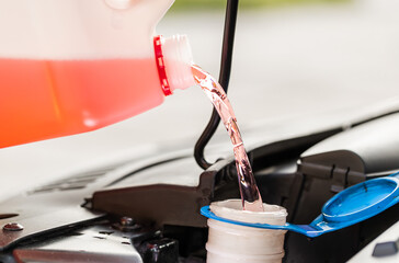 Close-up service worker man driver pouring red non freezing windshield cleaning glass washer fluid...