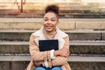 woman student e-learning distance training course study working on stairs in the city. African Ethnicity young woman watching online education webinar using a laptop