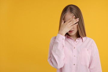Embarrassed woman covering face with hand on orange background, space for text