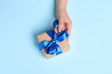 Woman holding gift box on light blue background, top view