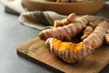 Many raw turmeric roots on grey table, closeup