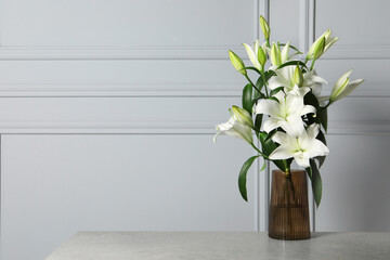 Beautiful bouquet of lily flowers in glass vase on light grey table, space for text