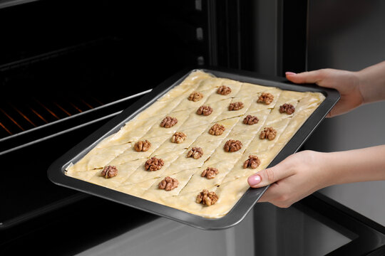 Woman putting baking pan with baklava into oven, closeup