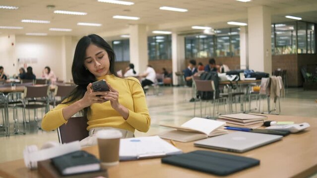 Asian woman using smartphone in library, College female student learning remotely.