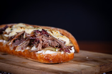 Shredded beef sandwich with caramelized onion, mustard sauce on wooden table. Delicious lunch