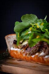 Shredded beef sandwich with arugula and caramelized onion, mustard sauce on wooden table. Delicious lunch
