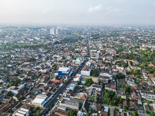 Aerial view of Jogja City with buildings, crowded vehicles traffic in morning sunlight. Population density is displacing agricultural land and forests.