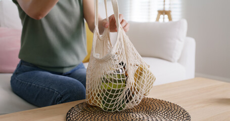 Young Gen Z girl asia people sit at home sofa couch unpack reuse mesh bag buy from eco friendly goods shop. Net zero waste bio go green life plastic free by refill glass bottle product retail store. - obrazy, fototapety, plakaty