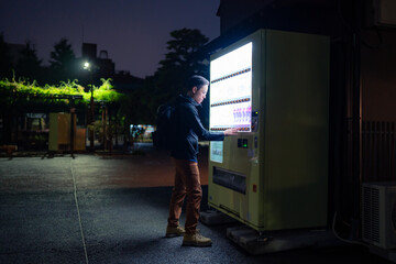 Side view of content Hispanic tourist male with backpack buying snack in vending machine on street...
