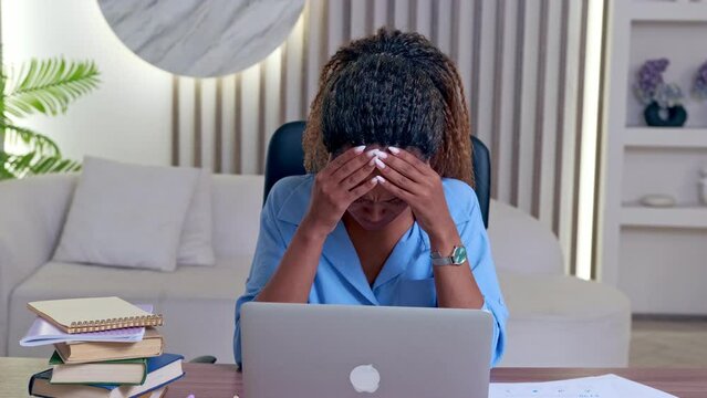 Young excited sad African American woman student who made mistake filling out online test for admission to college or university and feels panic after seeing result sits at table with laptop and books