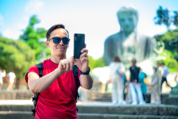 Happy young Hispanic male in casual red t-shirt with sunglasses and backpack taking selfie on...