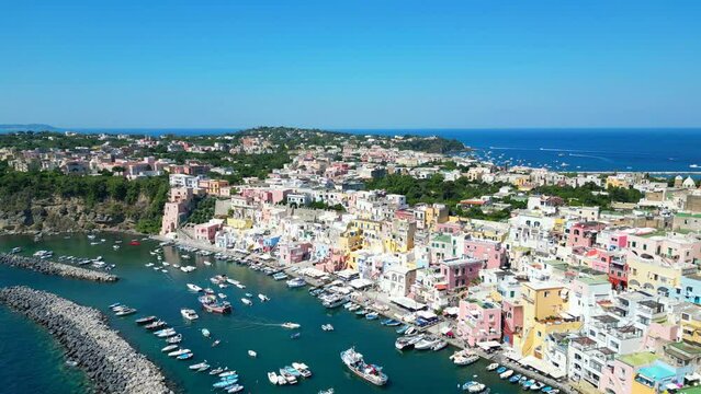 Ecstatic aerial pullback and pan right shot from Panoramica sulla Corricella on Procida Island (Isola di Procida) of the cobalt Tyrrhenian Sea in the Gulf of Naples with pastel buildings, white boats