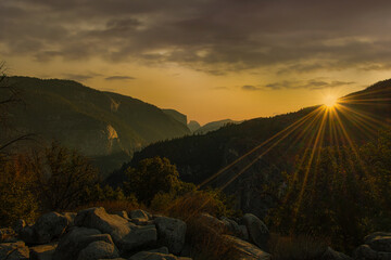 Sunburst on mountain top and half dome in the far background with rock formations of the Yosemite Valley 