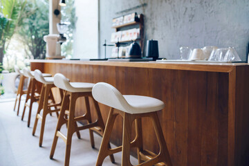 Seat and wooden counter with blur coffee equipment on counter bar and wooden shelf on rough cement wall with outdoor garden in background, Select focus at front chair
