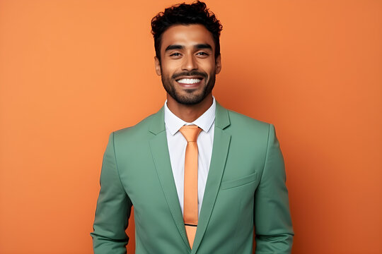 Handsome happy Indian man in green business suit on bright orange colour background, colourful studio portrait
