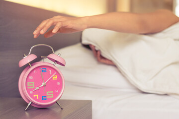 Women hand turn off the pink alarm clock on bed in morning.