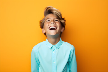 Colourful portrait of a young boy laughing and smiling wearing blue shirt on bright yellow background - obrazy, fototapety, plakaty