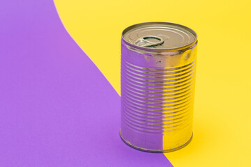Unopened Tin Can with Blank Edge on Split Yellow and Violet Background. Canned Food. Aluminum Can for Safe and Long Term Storage of Food. Steel Sealed Food Storage Container