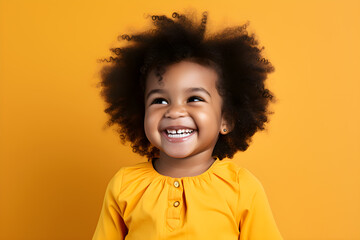 Portrait of a cute African American baby girl wearing yellow blouse laughing on bright yellow background