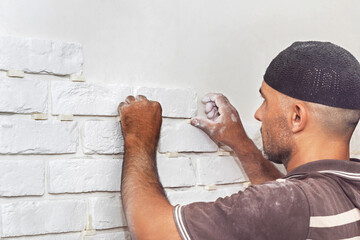 A man sticks a white decorative brick to the wall - obrazy, fototapety, plakaty