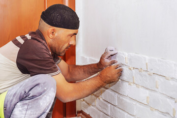 A man sticks a white decorative brick to the wall - obrazy, fototapety, plakaty