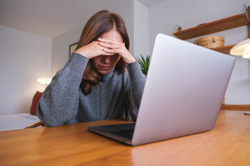 A woman get headache and stressed while working online on laptop computer at home