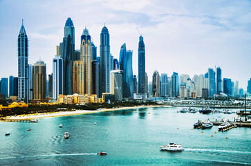 Fototapeta premium Dubai, United Arab Emirates, Dubai Marina area with famous skyscrapers, yachts and other landmarks at sunset with blue sky, view from Palm Jumeirah island