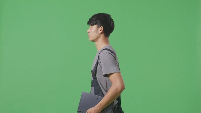 Side View Of Asian Man Worker Holding Tablet While Walking In The Green Screen Background Studio
