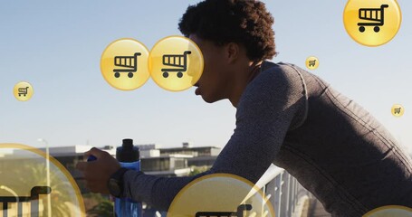 Animation of shopping cart icons, tired african american runner taking break and drinking water - Powered by Adobe