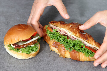 Close up image of a hand holding a sandwich. Bread with vegetables and ham.
