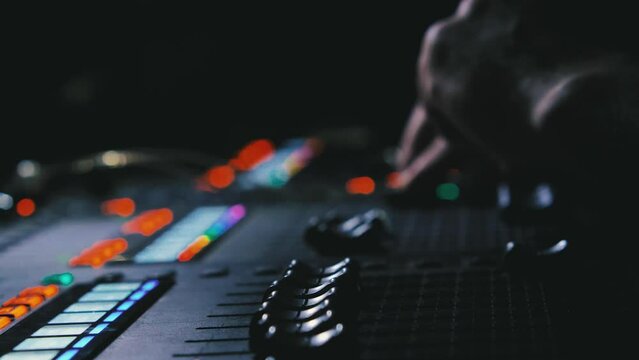 Sound engineer's fingers on the fader of a mixing console in a recording studio. Close-up. Music production is low key