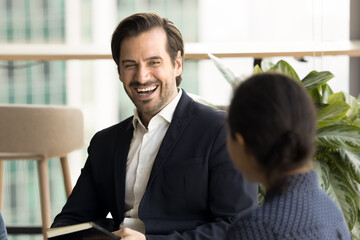 Happy male and female business colleagues discussing creative ideas for project, chatting, laughing, having fun on corporate meeting. Handsome businessman talking to coworker woman over shoulder view
