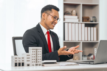 Agent presents contracts for property purchase or lease. Businessman asian indian people showcases miniature model home, signifying secure property insurance. Desk scene in a home sales office.