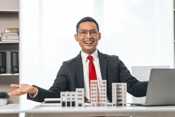 Agent presents contracts for property purchase or lease. Businessman asian indian people showcases miniature model home, signifying secure property insurance. Desk scene in a home sales office.