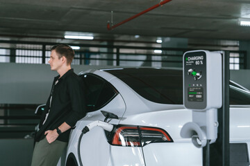 Young man travel with EV electric car to shopping center parking lot charging in downtown city...