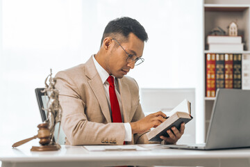 Middle-aged Asian indian people male lawyer meticulously reviews legal documents. Courtroom judge hammer and goddess scales. Depicting the essence of legal counseling and comprehensive services.