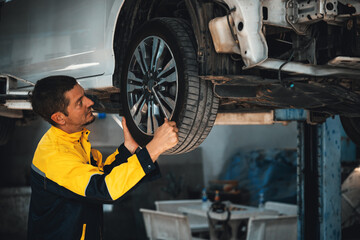 Hardworking mechanic changing car wheel under car lifting station. Automotive service worker changing leaking rubber tire in concept of professional car care and maintenance. Oxus