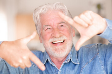 Portrait of cheerful attractive senior bearded man gesturing the camera frame with hands looking at the camera. Funny granfather expressing joy and happiness