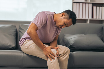 Middle-aged Asian Indian man with knee pain sitting on the sofa