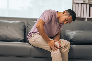 Middle-aged Asian Indian man with knee pain sitting on the sofa