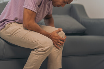 Middle-aged Asian Indian man with knee pain sitting on the sofa