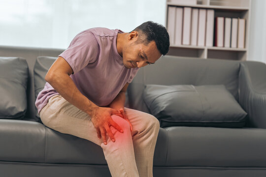 Middle-aged Asian Indian man with knee pain sitting on the sofa