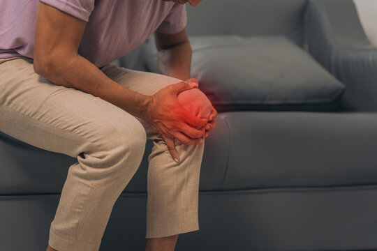Middle-aged Asian Indian man with knee pain sitting on the sofa