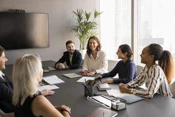 Happy positive multiethnic team brainstorming on project ideas together, talking at meeting table in boardroom, laughing at jokes, relaxing, having fun, discussing cooperation, working together