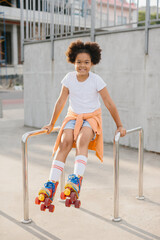 Fototapeta premium Cute young girl in roller skates having fun outdoors. The girl smiles looking at the camera.