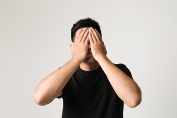 Stressed young Asian man cover his mouth with hands, posing over white wall.