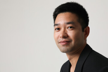 Close-up of smiling young Asian businessman in black suit isolated indoor.