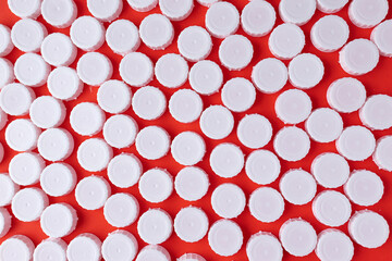 White plastic bottle screw caps on red  background. Recycling concept, waste sorting